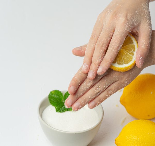 Young woman applying natural lemon scrub on hands against white
