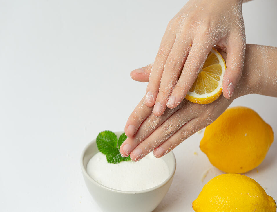 Young woman applying natural lemon scrub on hands against white Young woman applying natural lemon scrub on hands against white